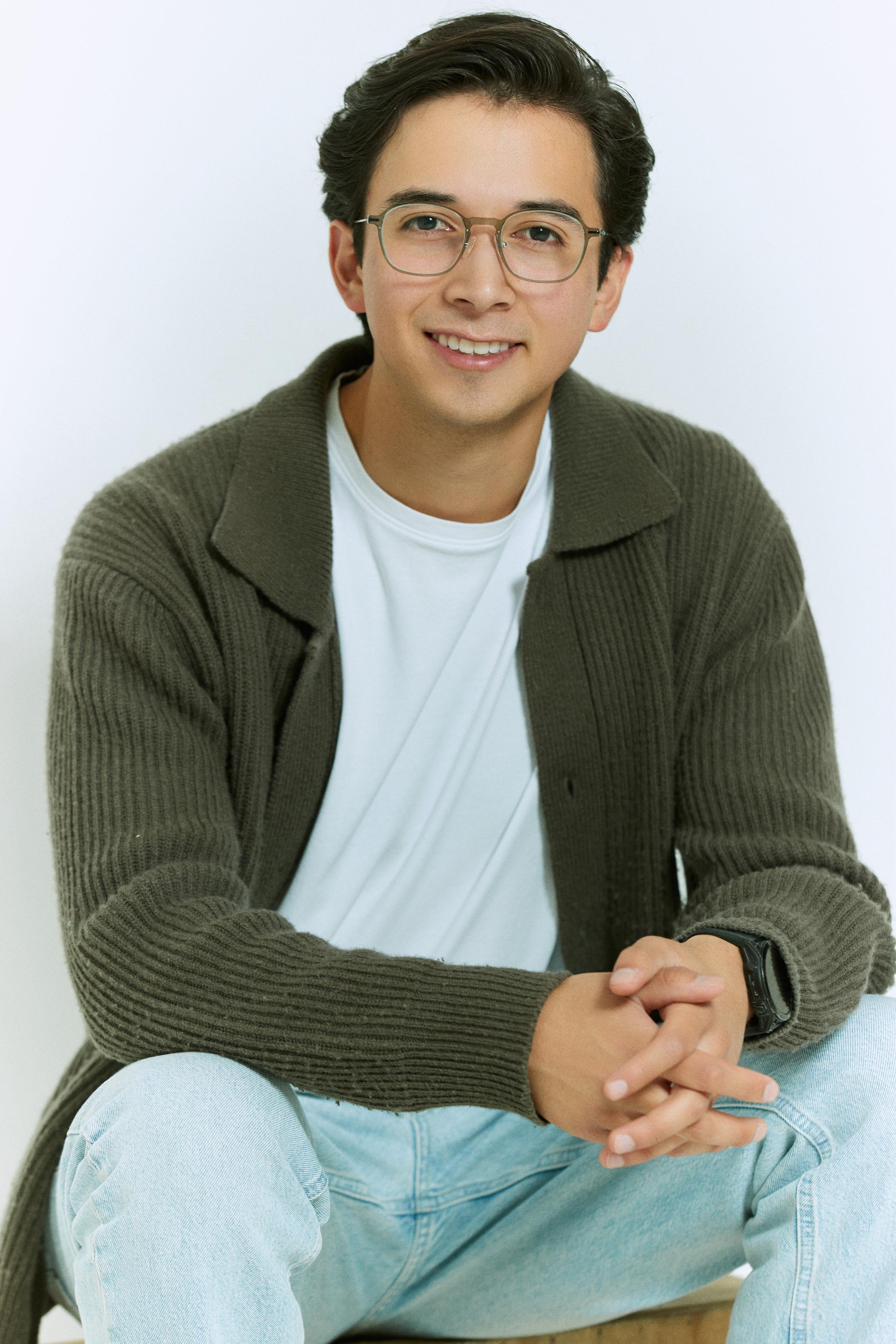 Retrato de Ángel Santana sentado, sonriendo, con lentes y suéter verde olivo